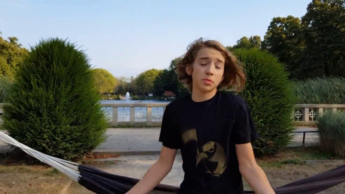 Teenie auf einer Hängematte sitzend, er zuckt mit den Schultern, er trägt ein schwarzes T-Shirt mit einem Penguin mit Startschuss-Pistole in gold mit einer Schablone gesprüht