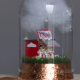Foto einer Miniatur: eine rot-weiße Popcorn-Bude, die auf einer Wiese unter einer weißen Wolke steht, geschützt von einer Glaskuppel, auf einem rotgoldenem Sockel
