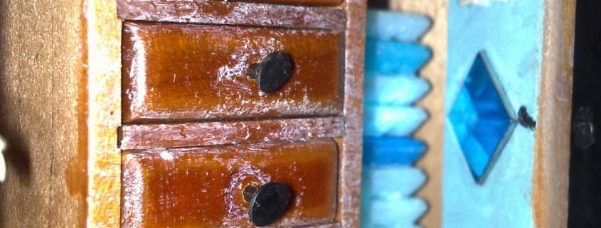 Detailansichten eines Schaukastens mit Elementen aus Holz, Glas, Metall und Miniaturen aus dem Alltag. Neben Holzfarben ist die dominierende Farbe ein helles Blau.