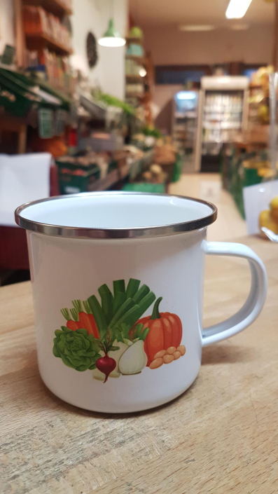 Tasse aus weißen Emaille bedruckt mit Gemüse auf der Theke im Gemüseladen